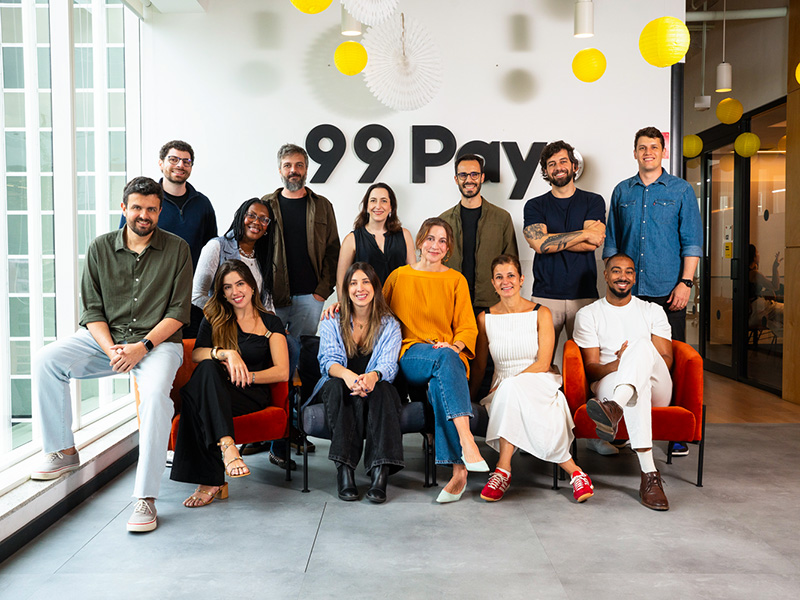 En el centro están Fernanda Tedde, CEO de Fbiz (sentada), y Marina Beer, directora de Marketing de 99Pay (de pie), junto a los equipos de Fbiz y 99Pay.